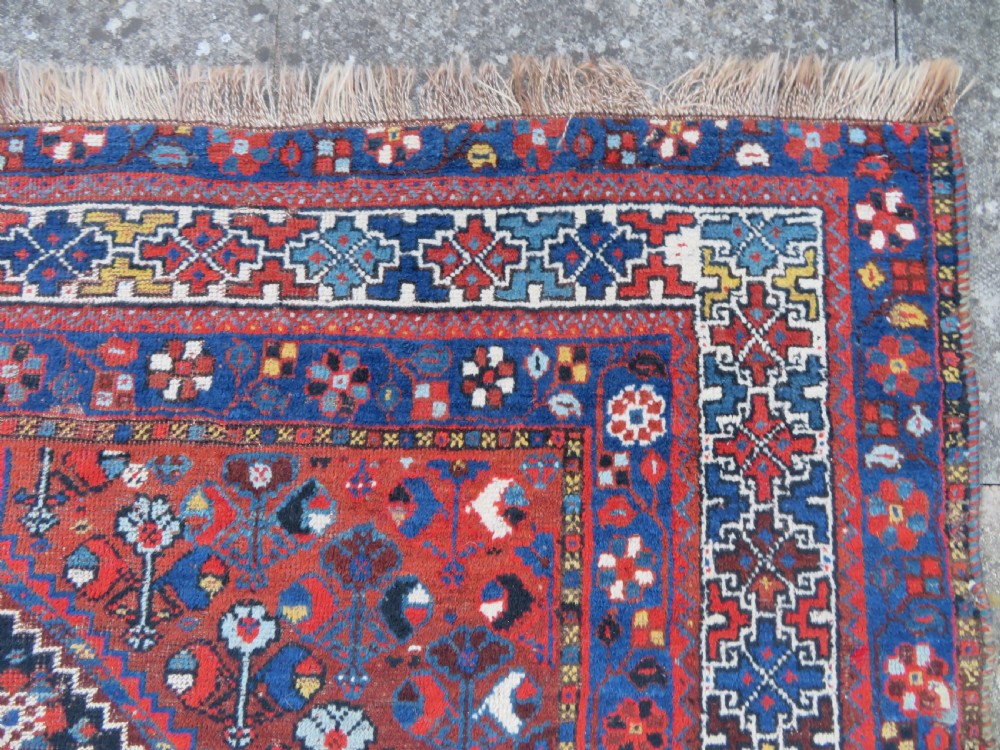 An antique Persian Khamseh wool carpet featuring a dark navy blue field with three stacked diamond medallions and geometric borders in terracotta red and ivory. View XI