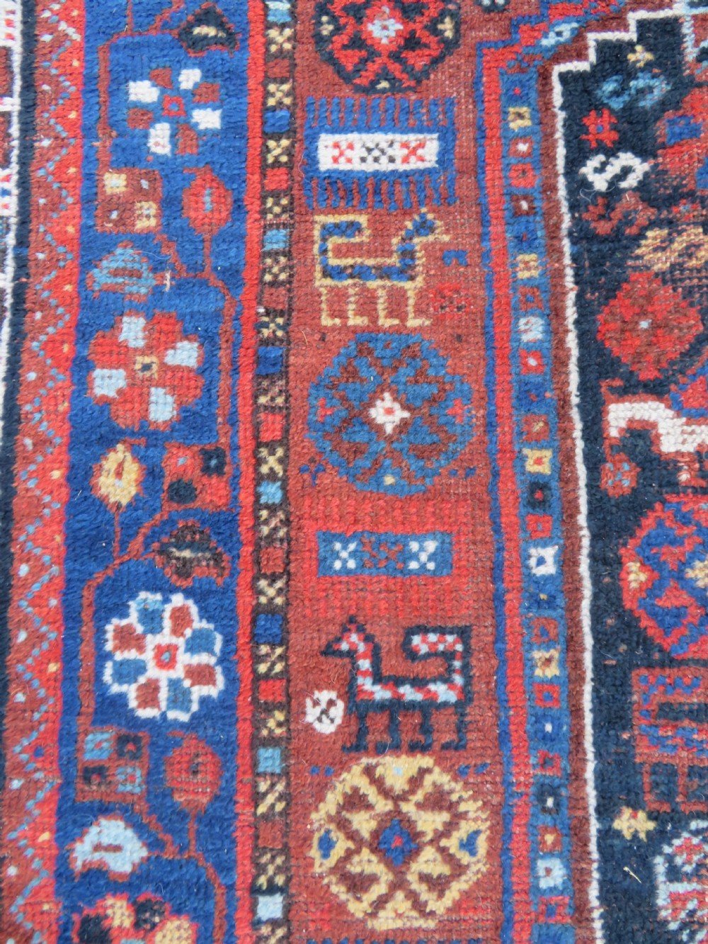 An antique Persian Khamseh wool carpet featuring a dark navy blue field with three stacked diamond medallions and geometric borders in terracotta red and ivory. View XVIII