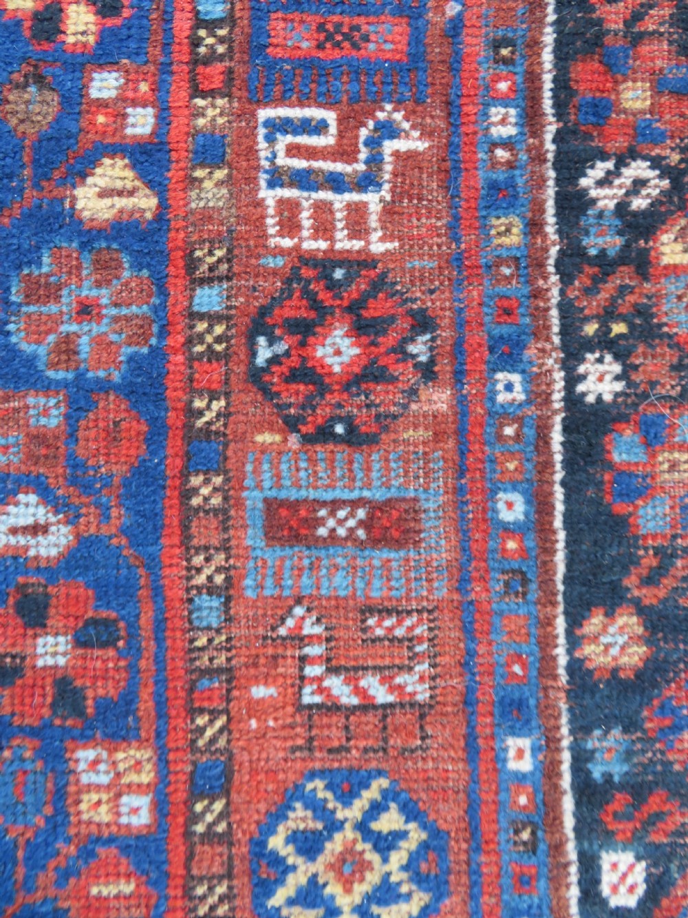 An antique Persian Khamseh wool carpet featuring a dark navy blue field with three stacked diamond medallions and geometric borders in terracotta red and ivory. View XIX