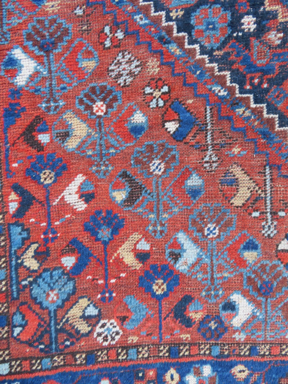 An antique Persian Khamseh wool carpet featuring a dark navy blue field with three stacked diamond medallions and geometric borders in terracotta red and ivory. View XX