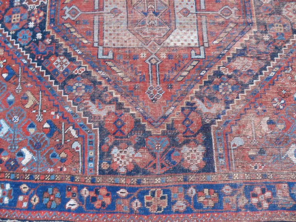 An antique Persian Khamseh wool carpet featuring a dark navy blue field with three stacked diamond medallions and geometric borders in terracotta red and ivory. View XXI