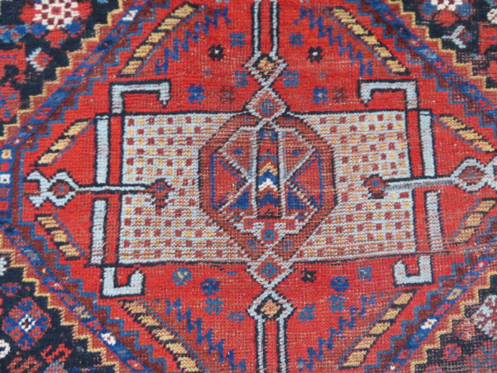 An antique Persian Khamseh wool carpet featuring a dark navy blue field with three stacked diamond medallions and geometric borders in terracotta red and ivory. View XXIV
