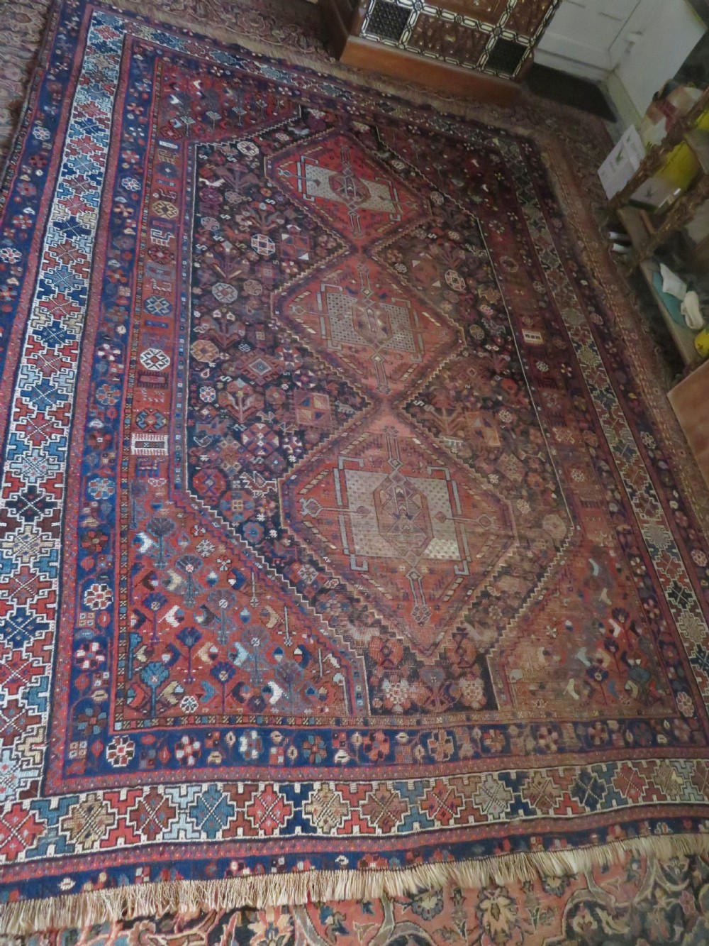 An antique Persian Khamseh wool carpet featuring a dark navy blue field with three stacked diamond medallions and geometric borders in terracotta red and ivory. View XXIX