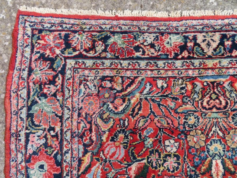 An antique hand-knotted Persian Sarouk wool rug featuring a red field with a central navy medallion and dense floral motifs within a dark border. View VIII