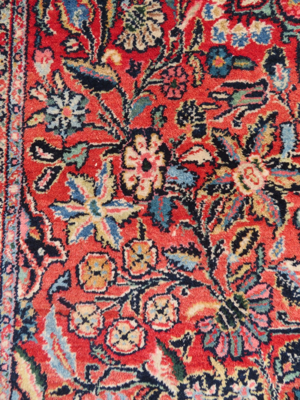 An antique hand-knotted Persian Sarouk wool rug featuring a red field with a central navy medallion and dense floral motifs within a dark border. View IX