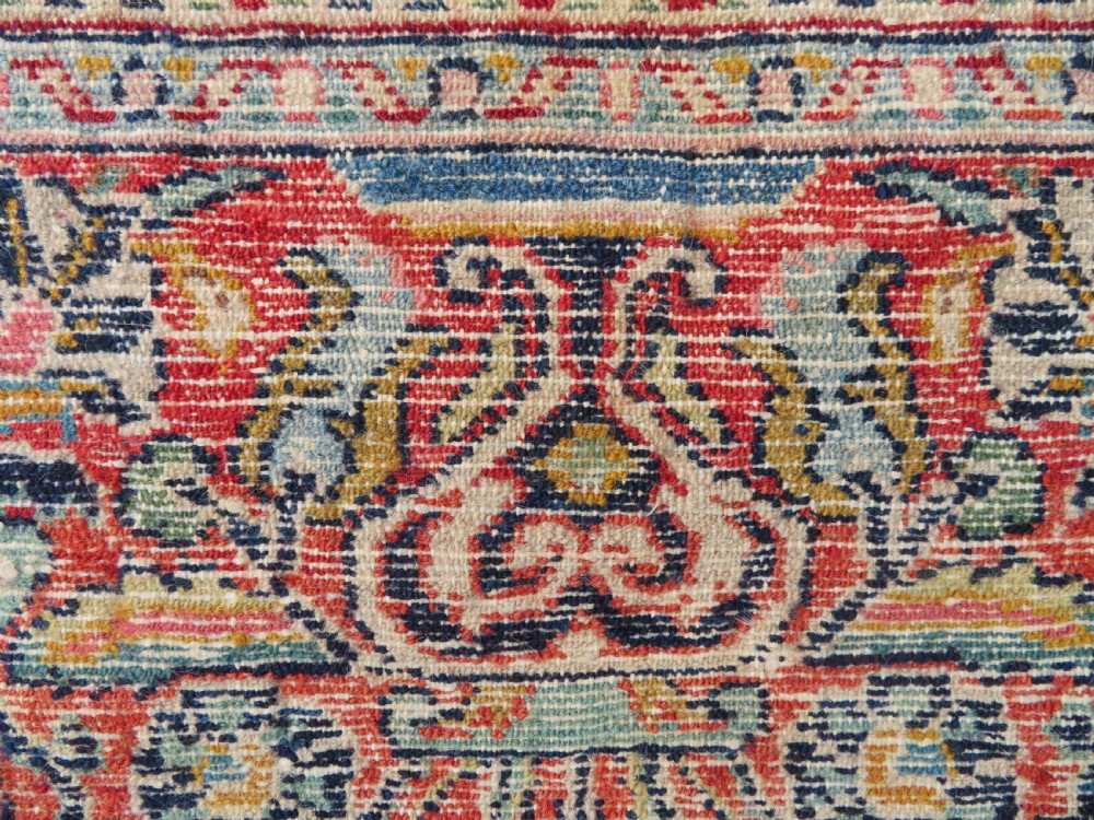 An antique hand-knotted Persian Sarouk wool rug featuring a red field with a central navy medallion and dense floral motifs within a dark border. View XVI