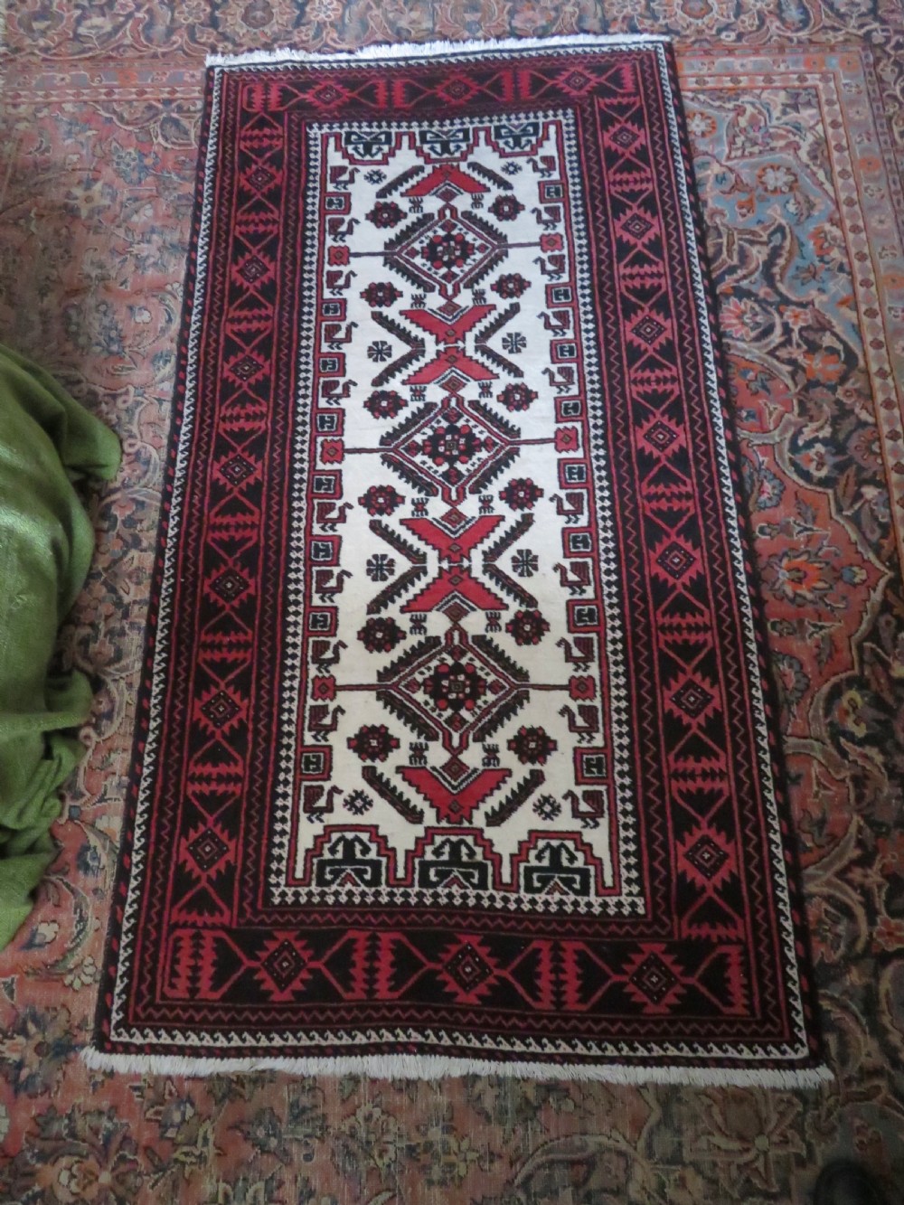 A rectangular hand-knotted wool Baluch rug featuring a central cream field with red geometric diamond motifs surrounded by a dark geometric border. View XIII
