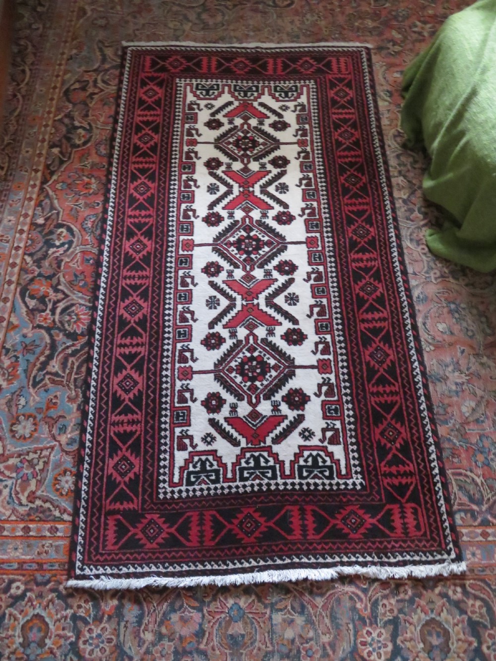 A rectangular hand-knotted wool Baluch rug featuring a central cream field with red geometric diamond motifs surrounded by a dark geometric border. View XIV