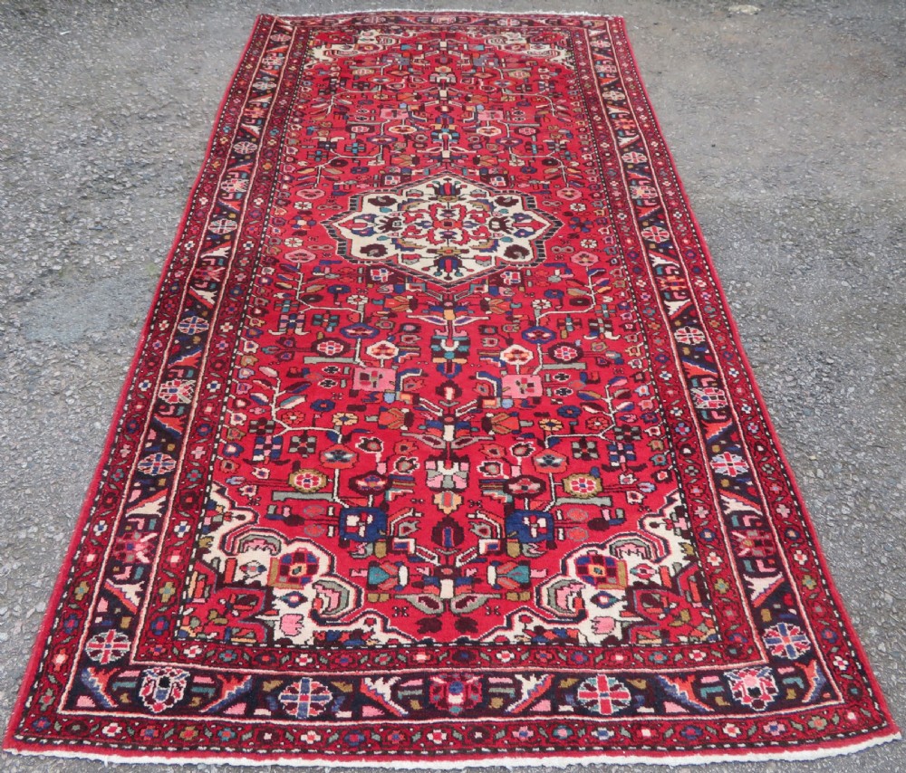 A long hand-knotted Persian Hamadan Kelleh carpet featuring a central cream medallion surrounded by geometric and floral motifs on a red field with multi-tiered borders.