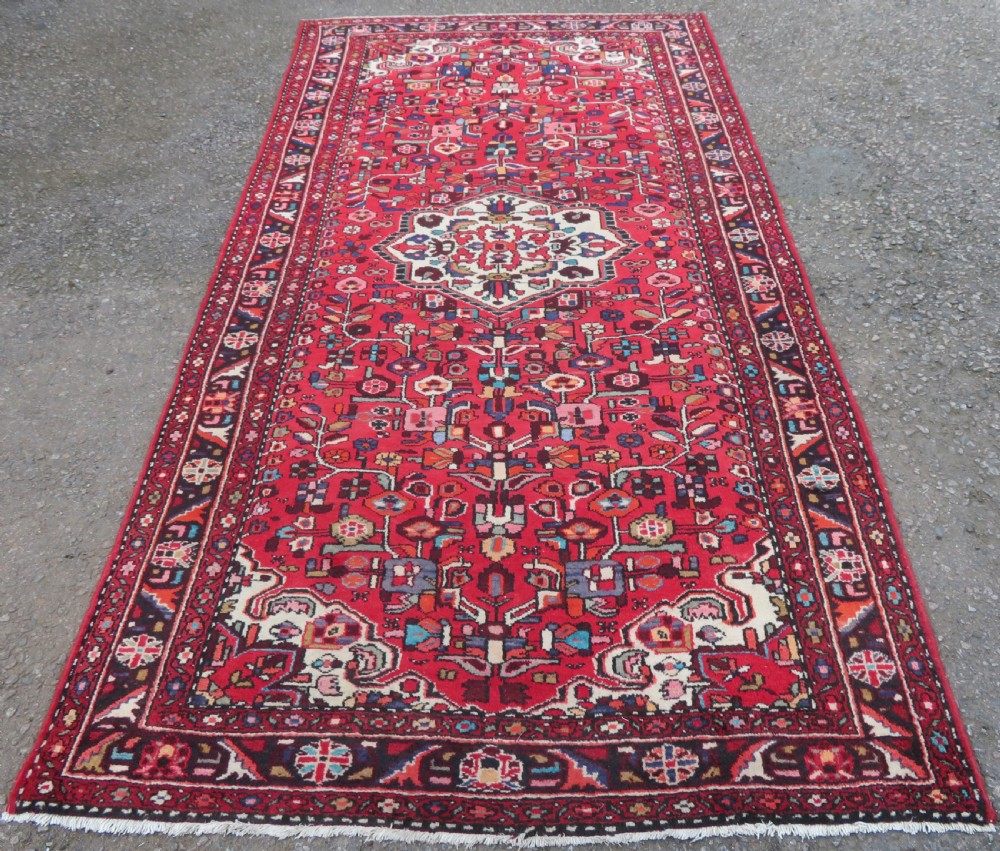 A long hand-knotted Persian Hamadan Kelleh carpet featuring a central cream medallion surrounded by geometric and floral motifs on a red field with multi-tiered borders. View II