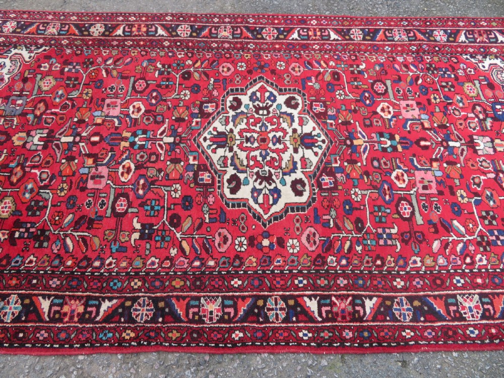 A long hand-knotted Persian Hamadan Kelleh carpet featuring a central cream medallion surrounded by geometric and floral motifs on a red field with multi-tiered borders. View III