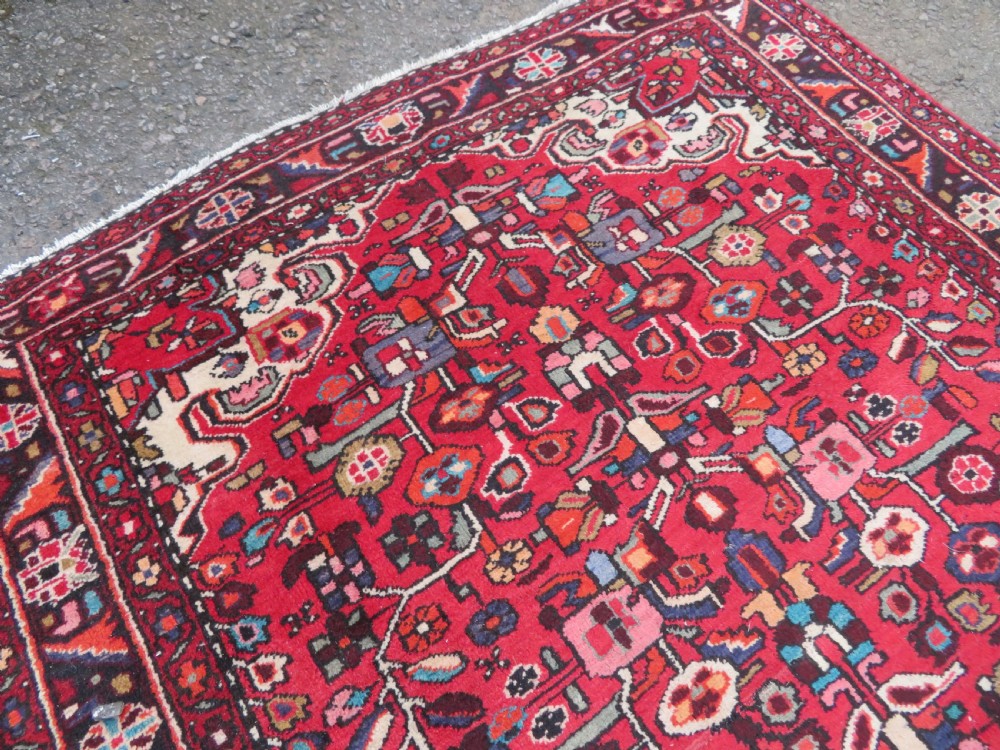 A long hand-knotted Persian Hamadan Kelleh carpet featuring a central cream medallion surrounded by geometric and floral motifs on a red field with multi-tiered borders. View IV