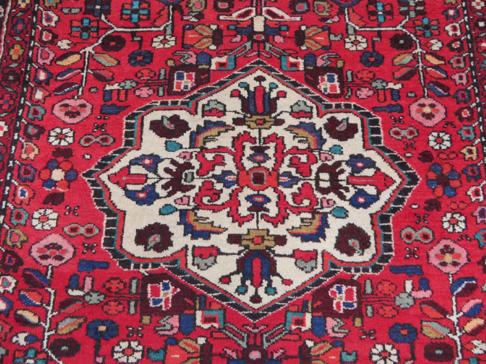A long hand-knotted Persian Hamadan Kelleh carpet featuring a central cream medallion surrounded by geometric and floral motifs on a red field with multi-tiered borders. View V