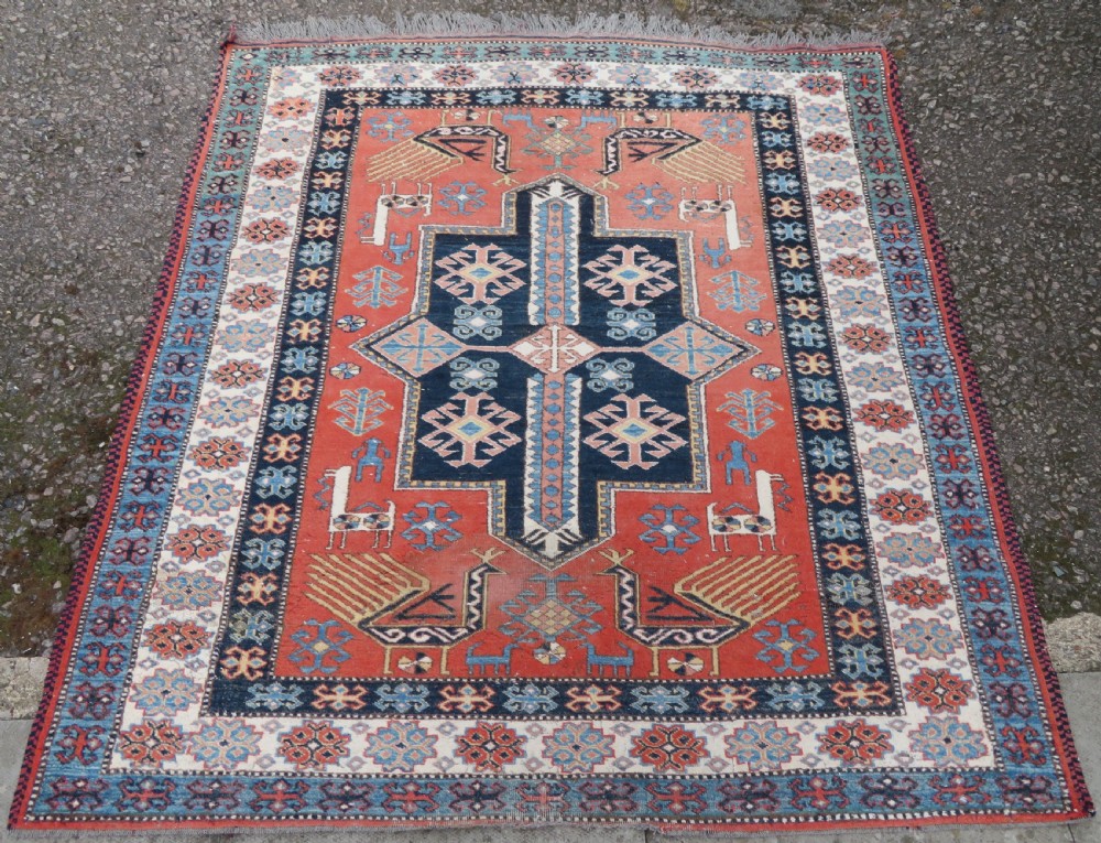 A handwoven rectangular wool rug featuring a central navy blue stepped medallion and a terracotta field decorated with peacock and animal motifs. View II