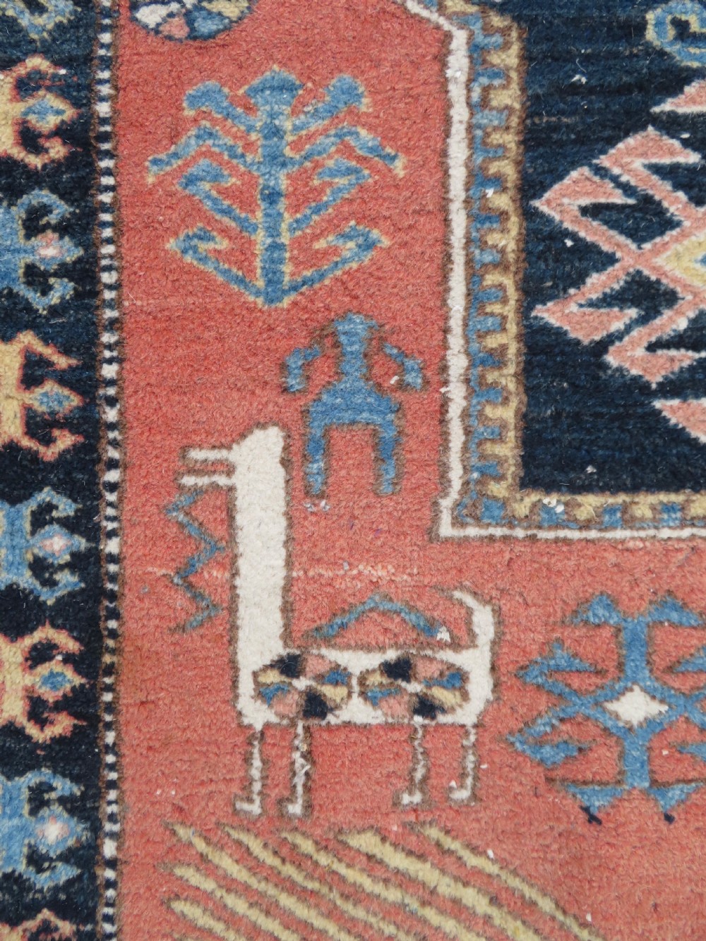 A handwoven rectangular wool rug featuring a central navy blue stepped medallion and a terracotta field decorated with peacock and animal motifs. View VII