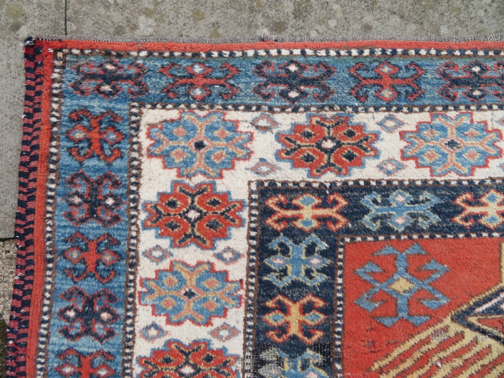 A handwoven rectangular wool rug featuring a central navy blue stepped medallion and a terracotta field decorated with peacock and animal motifs. View VIII
