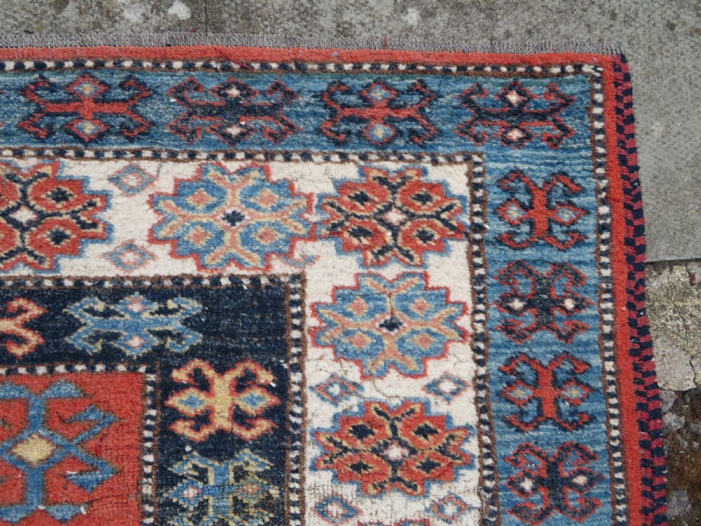 A handwoven rectangular wool rug featuring a central navy blue stepped medallion and a terracotta field decorated with peacock and animal motifs. View X