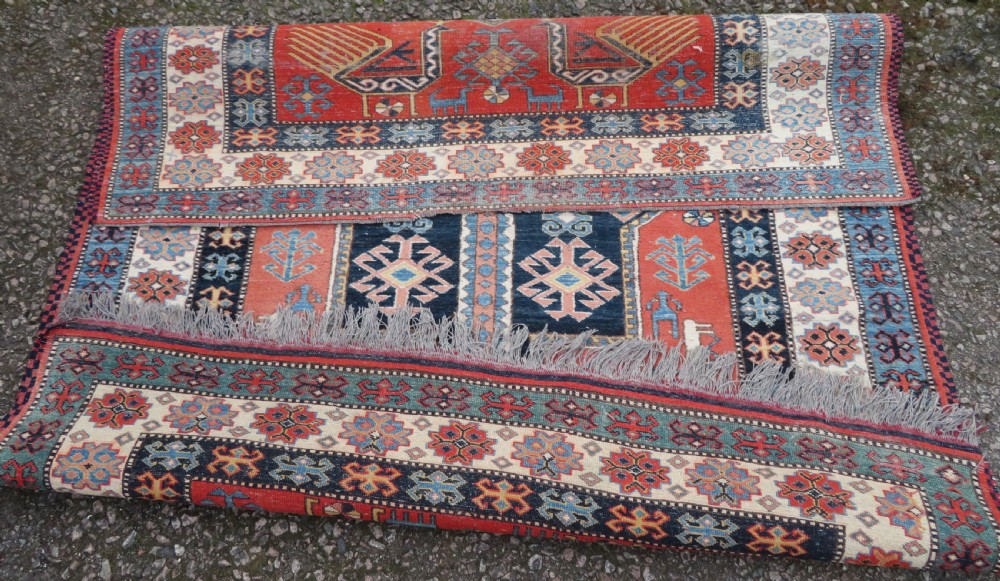 A handwoven rectangular wool rug featuring a central navy blue stepped medallion and a terracotta field decorated with peacock and animal motifs. View XVII