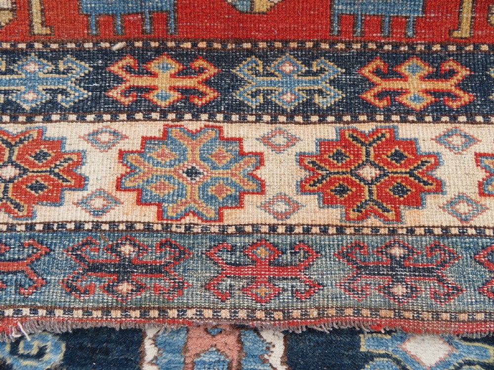 A handwoven rectangular wool rug featuring a central navy blue stepped medallion and a terracotta field decorated with peacock and animal motifs. View XIX