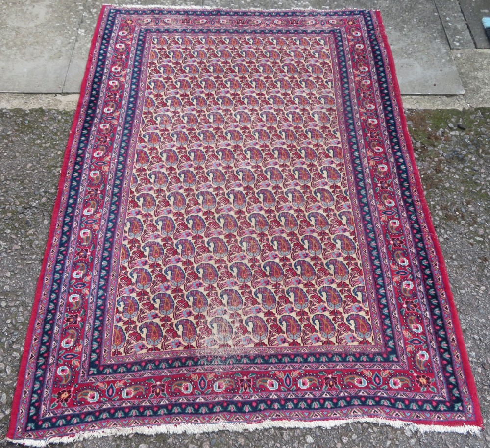 An antique Persian Meshed Doroksh wool rug featuring a repeating all-over boteh pattern on a cream field within multi-banded crimson and navy borders.