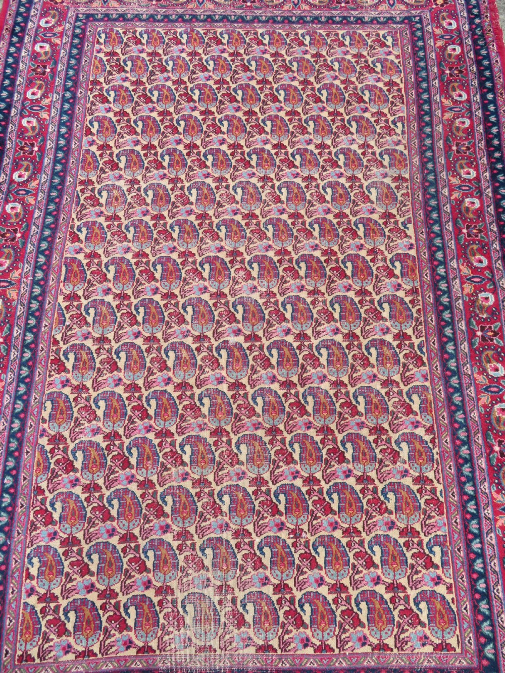 An antique Persian Meshed Doroksh wool rug featuring a repeating all-over boteh pattern on a cream field within multi-banded crimson and navy borders. View III