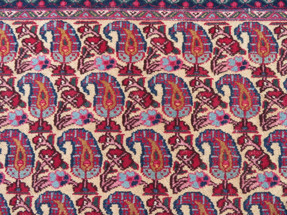 An antique Persian Meshed Doroksh wool rug featuring a repeating all-over boteh pattern on a cream field within multi-banded crimson and navy borders. View IV