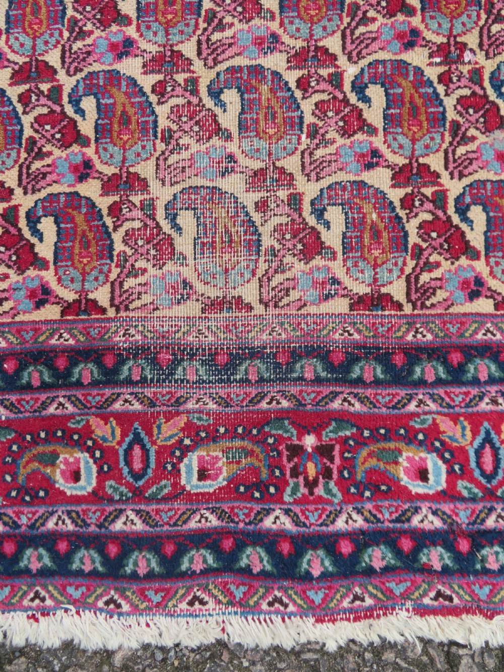 An antique Persian Meshed Doroksh wool rug featuring a repeating all-over boteh pattern on a cream field within multi-banded crimson and navy borders. View V