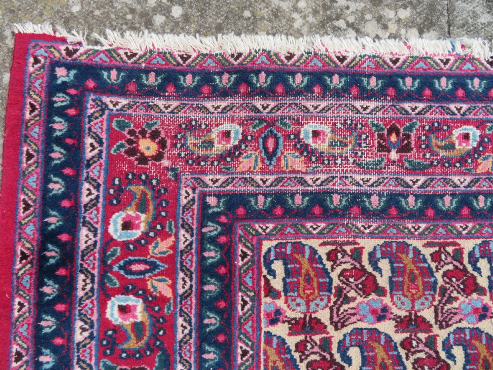 An antique Persian Meshed Doroksh wool rug featuring a repeating all-over boteh pattern on a cream field within multi-banded crimson and navy borders. View VIII
