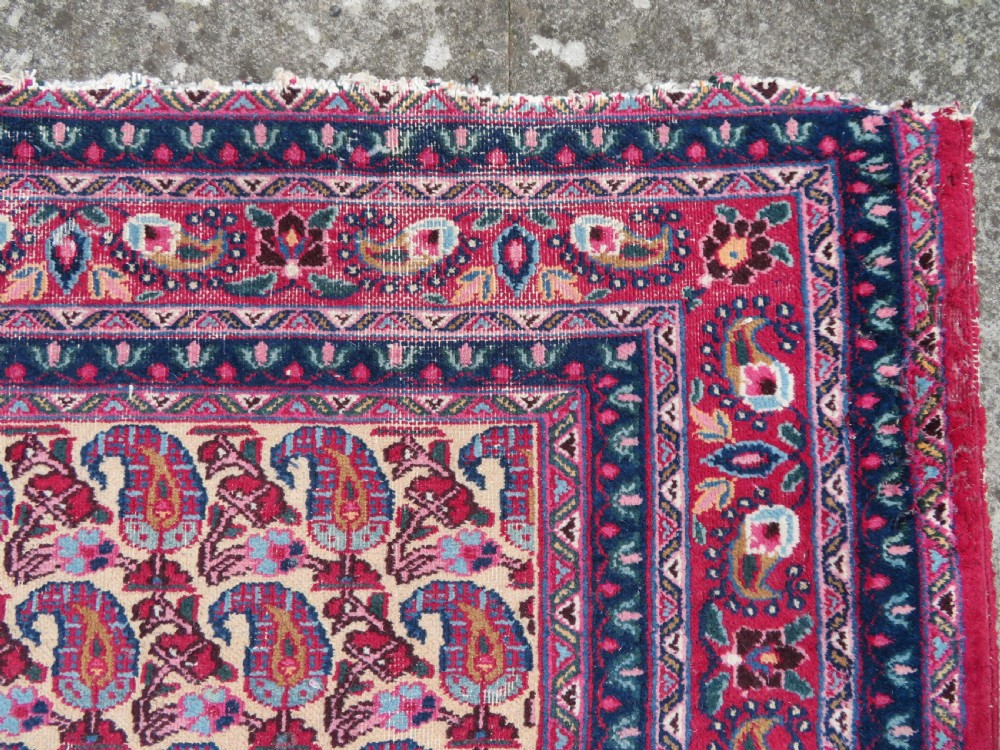 An antique Persian Meshed Doroksh wool rug featuring a repeating all-over boteh pattern on a cream field within multi-banded crimson and navy borders. View IX