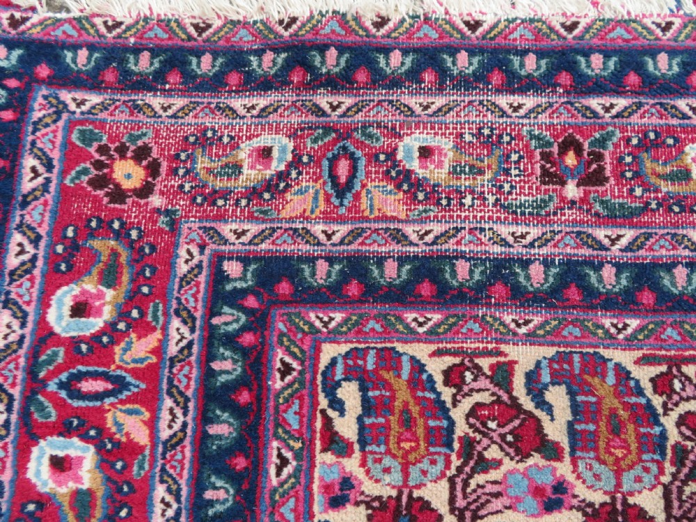 An antique Persian Meshed Doroksh wool rug featuring a repeating all-over boteh pattern on a cream field within multi-banded crimson and navy borders. View X