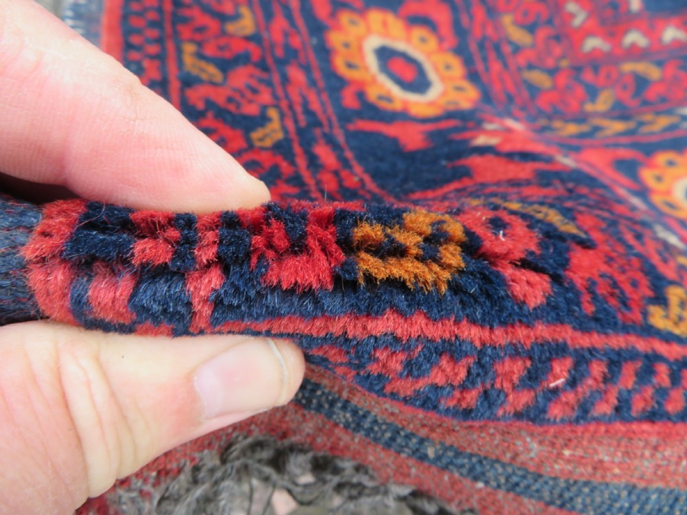 A rectangular hand-knotted wool rug featuring two central dark blue geometric medallions on a deep red field framed by decorated floral borders and fringe ends. View IV