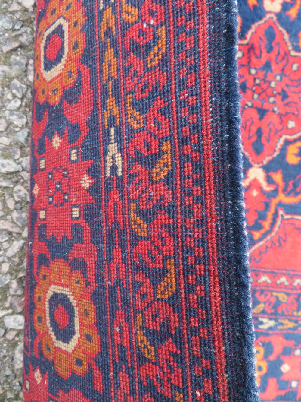 A rectangular hand-knotted wool rug featuring two central dark blue geometric medallions on a deep red field framed by decorated floral borders and fringe ends. View VI