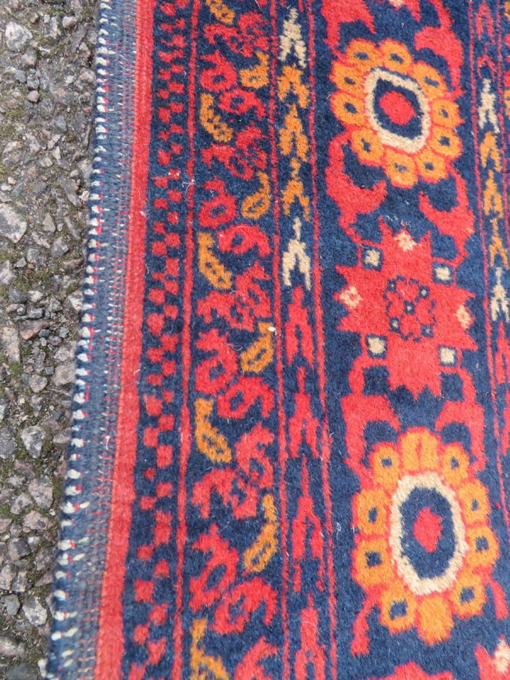 A rectangular hand-knotted wool rug featuring two central dark blue geometric medallions on a deep red field framed by decorated floral borders and fringe ends. View VII