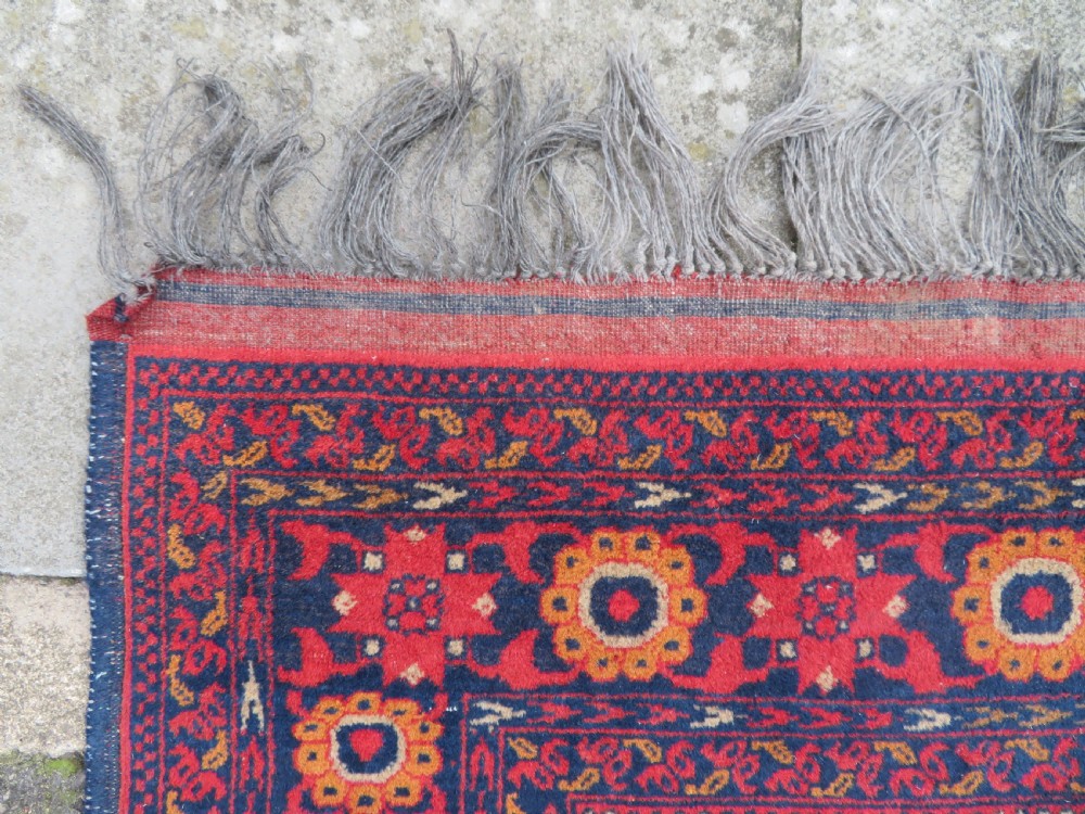A rectangular hand-knotted wool rug featuring two central dark blue geometric medallions on a deep red field framed by decorated floral borders and fringe ends. View VIII