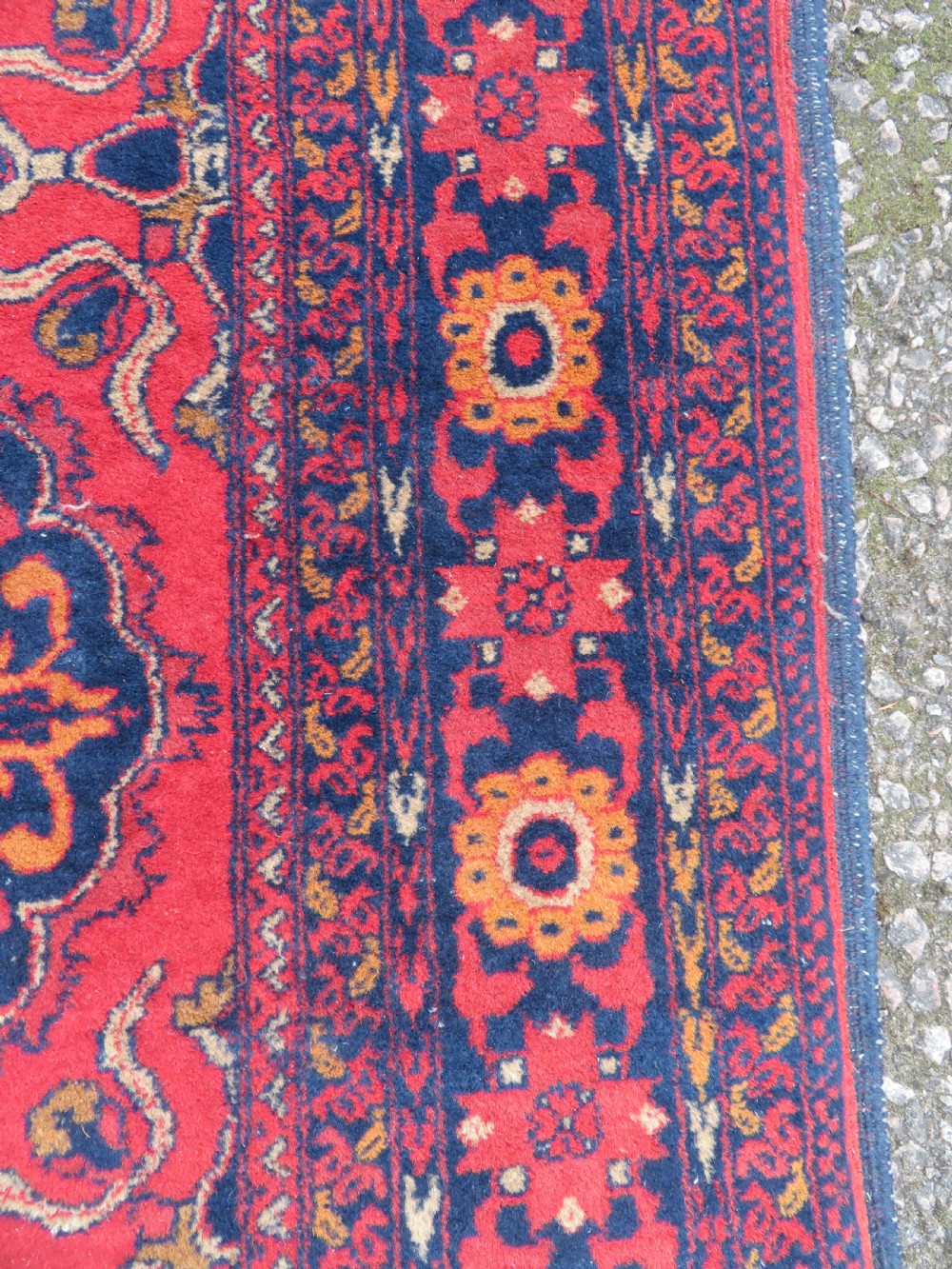 A rectangular hand-knotted wool rug featuring two central dark blue geometric medallions on a deep red field framed by decorated floral borders and fringe ends. View IX