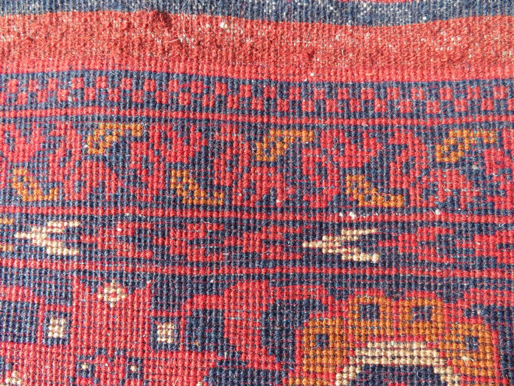 A rectangular hand-knotted wool rug featuring two central dark blue geometric medallions on a deep red field framed by decorated floral borders and fringe ends. View XIV