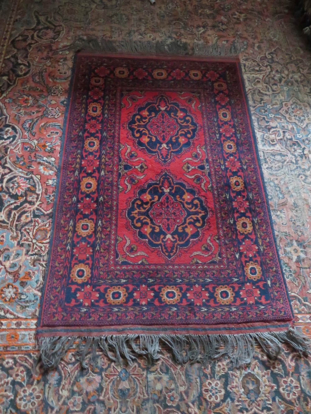 A rectangular hand-knotted wool rug featuring two central dark blue geometric medallions on a deep red field framed by decorated floral borders and fringe ends. View XV