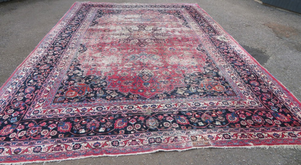A large hand-knotted Persian Sarouk wool carpet featuring a distressed rose red field, central floral medallion, and deep navy blue floral borders. View III