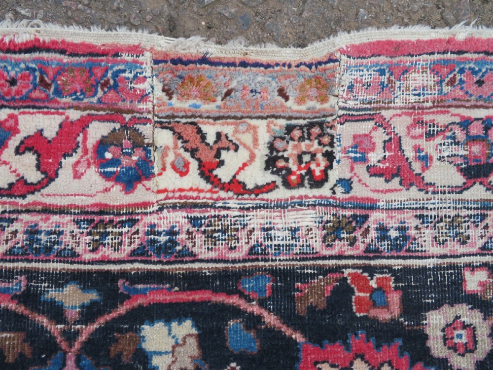 A large hand-knotted Persian Sarouk wool carpet featuring a distressed rose red field, central floral medallion, and deep navy blue floral borders. View X
