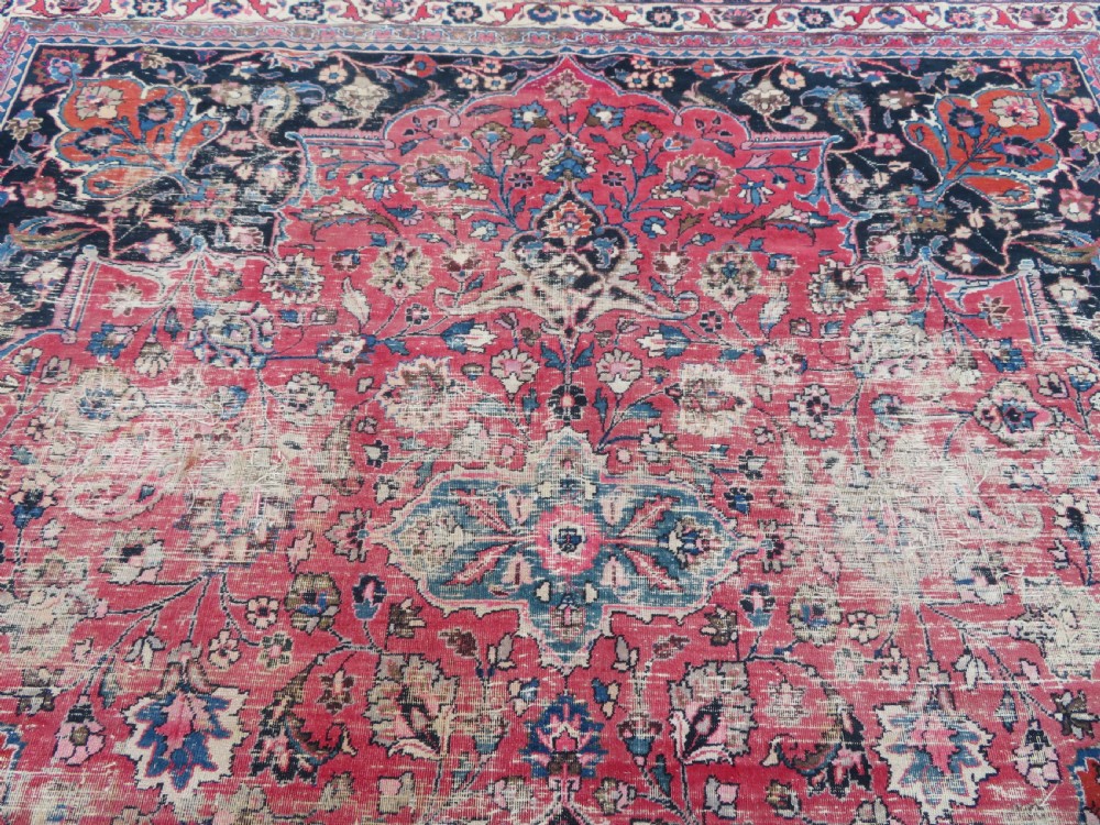 A large hand-knotted Persian Sarouk wool carpet featuring a distressed rose red field, central floral medallion, and deep navy blue floral borders. View XIII