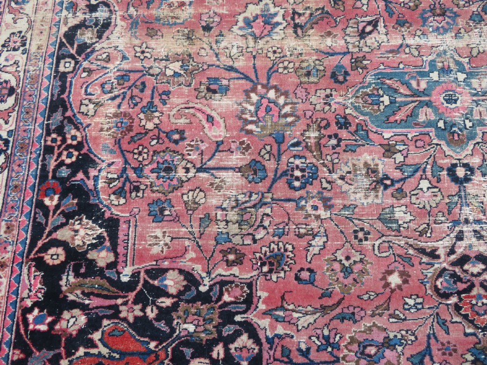A large hand-knotted Persian Sarouk wool carpet featuring a distressed rose red field, central floral medallion, and deep navy blue floral borders. View XVII