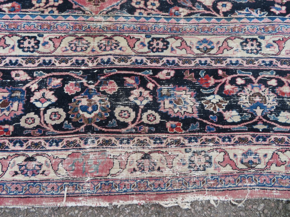 A large hand-knotted Persian Sarouk wool carpet featuring a distressed rose red field, central floral medallion, and deep navy blue floral borders. View XVIII