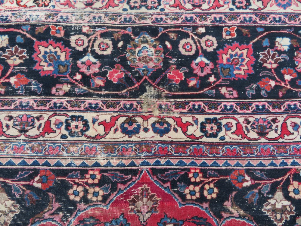 A large hand-knotted Persian Sarouk wool carpet featuring a distressed rose red field, central floral medallion, and deep navy blue floral borders. View XX