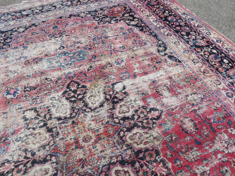 A large hand-knotted Persian Sarouk wool carpet featuring a distressed rose red field, central floral medallion, and deep navy blue floral borders. View XXII