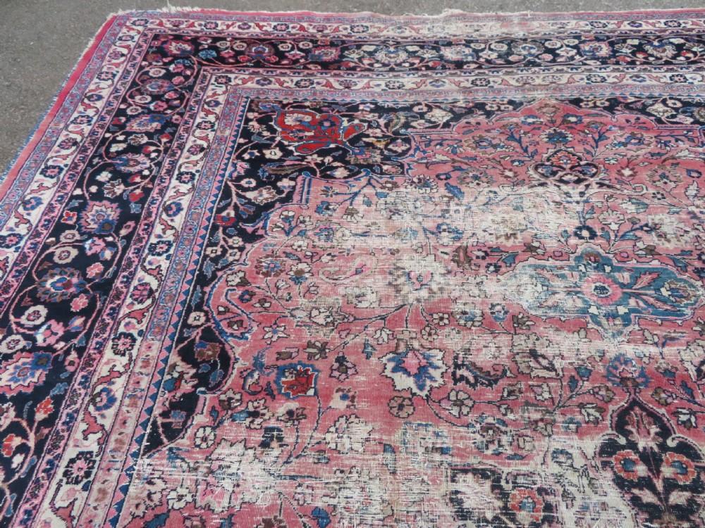 A large hand-knotted Persian Sarouk wool carpet featuring a distressed rose red field, central floral medallion, and deep navy blue floral borders. View XXIV