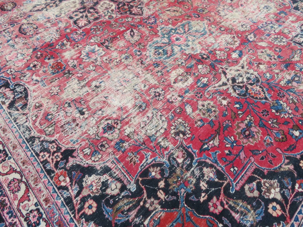 A large hand-knotted Persian Sarouk wool carpet featuring a distressed rose red field, central floral medallion, and deep navy blue floral borders. View XXVI