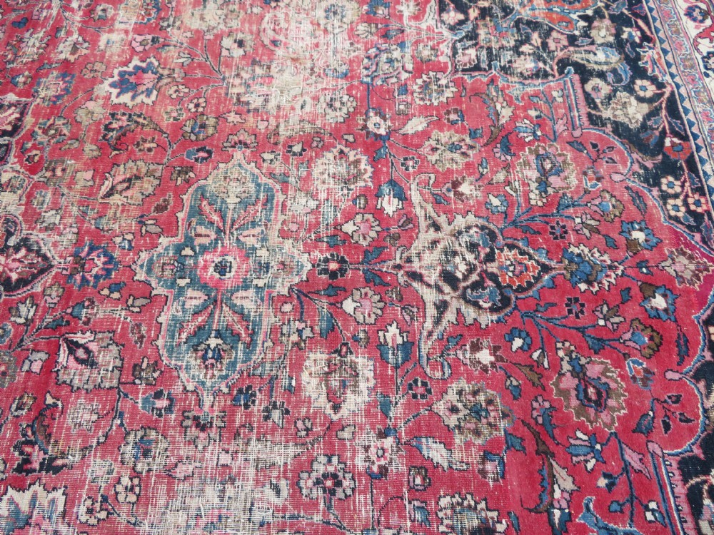 A large hand-knotted Persian Sarouk wool carpet featuring a distressed rose red field, central floral medallion, and deep navy blue floral borders. View XXVII
