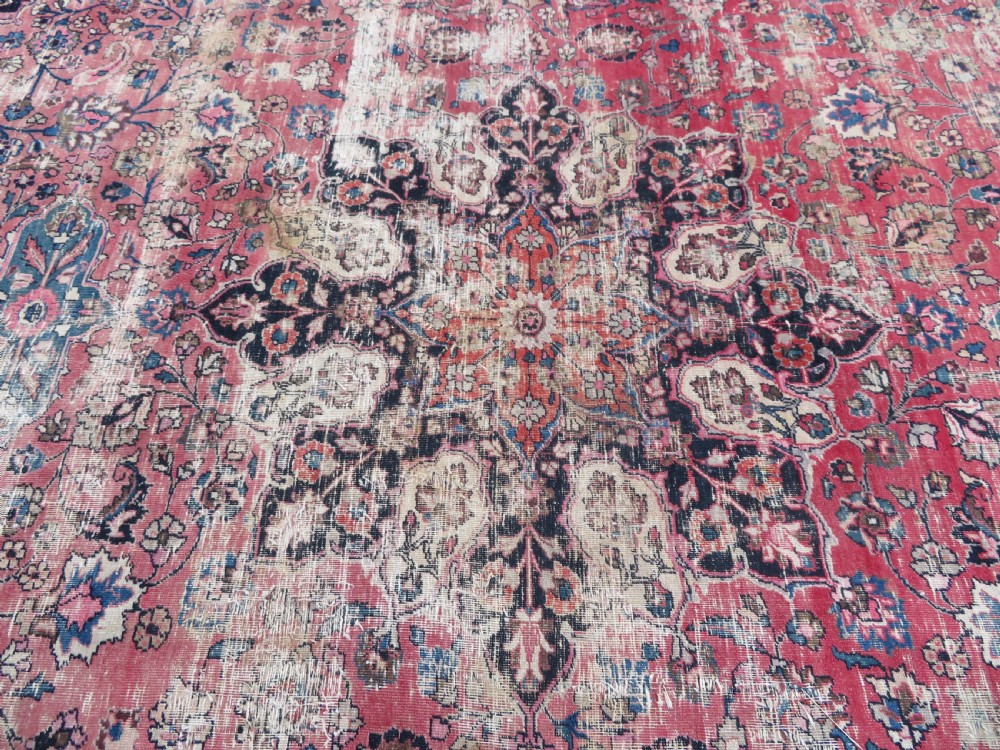 A large hand-knotted Persian Sarouk wool carpet featuring a distressed rose red field, central floral medallion, and deep navy blue floral borders. View XXVIII