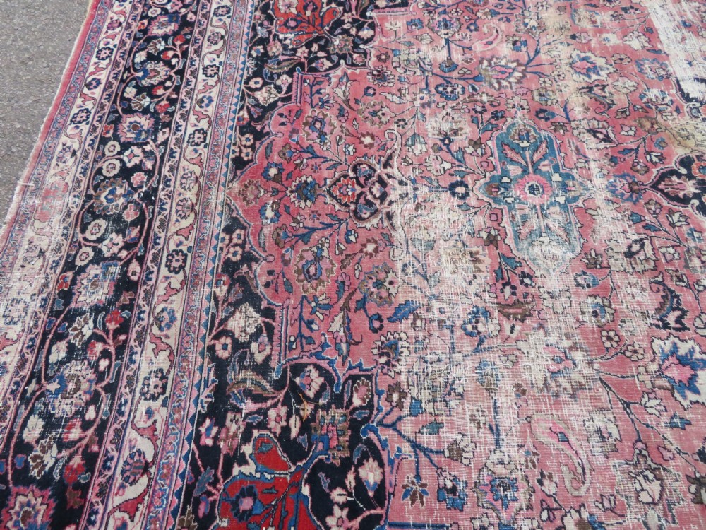 A large hand-knotted Persian Sarouk wool carpet featuring a distressed rose red field, central floral medallion, and deep navy blue floral borders. View XXIX