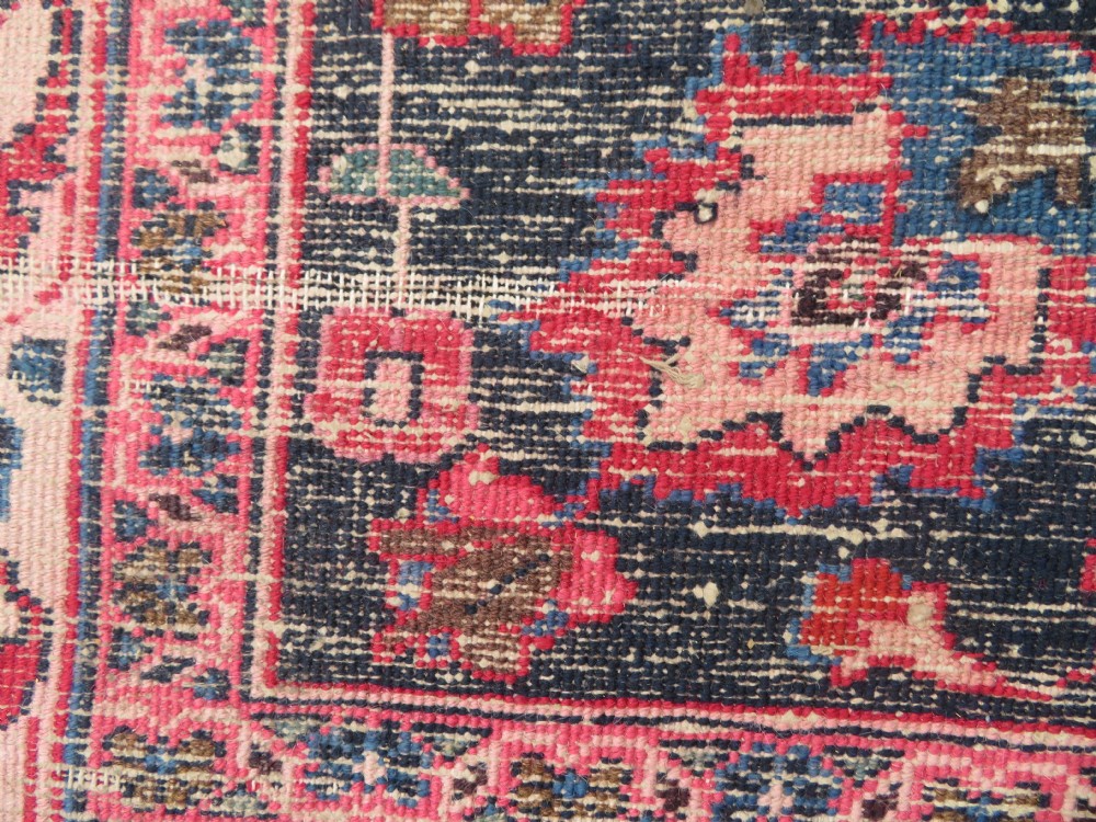 A large hand-knotted Persian Sarouk wool carpet featuring a distressed rose red field, central floral medallion, and deep navy blue floral borders. View XXXI